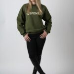 Woman in green sweatshirt and black pants posing against a plain background.