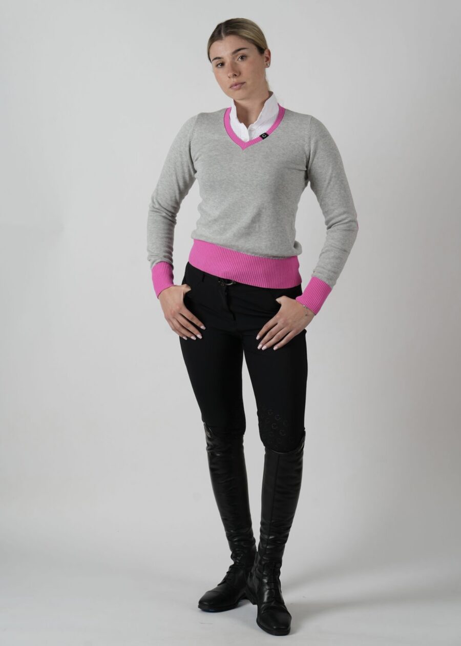 Person wearing a gray sweater over a pink shirt with black pants.