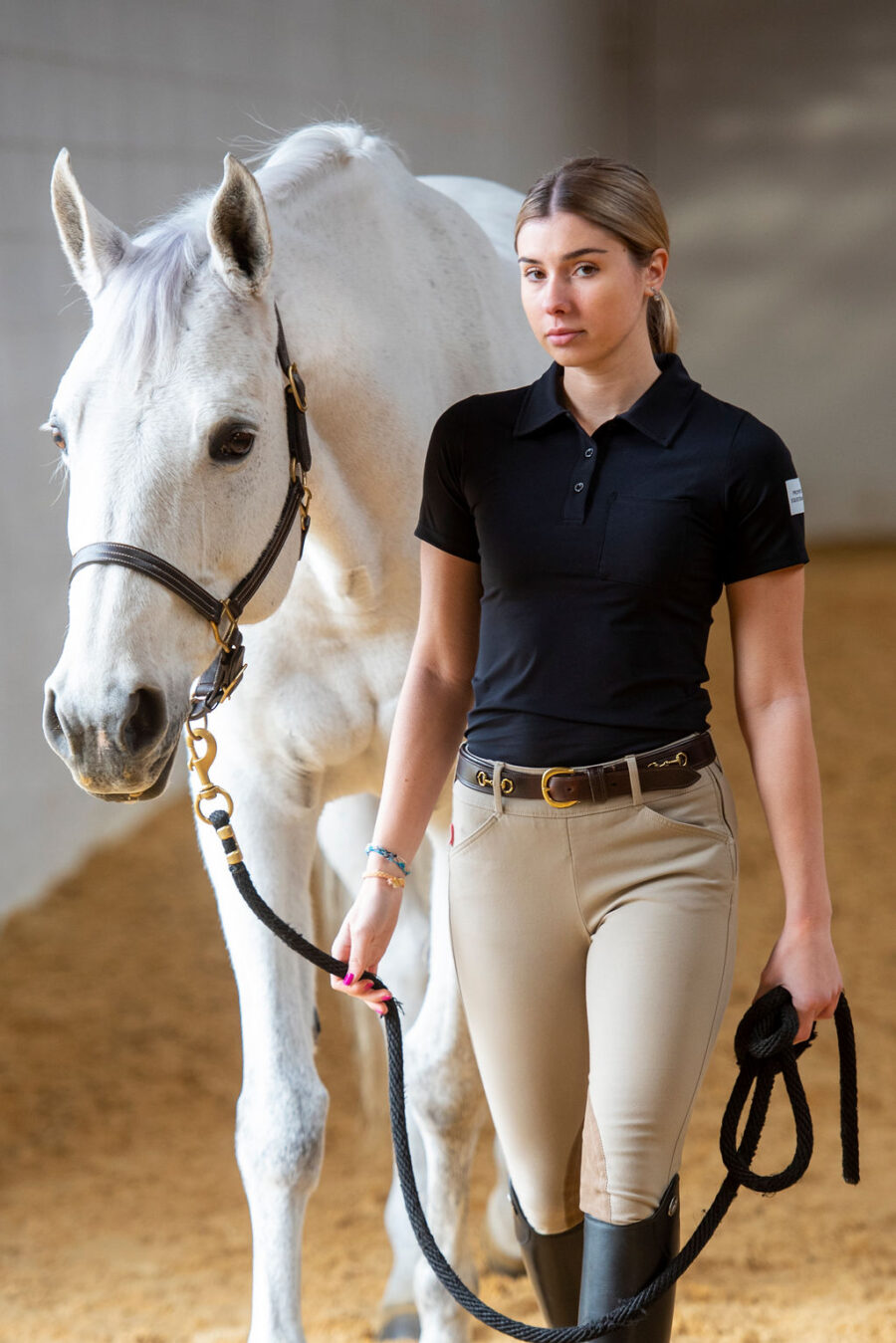 A woman in equestrian attire holding a white horse's reins.