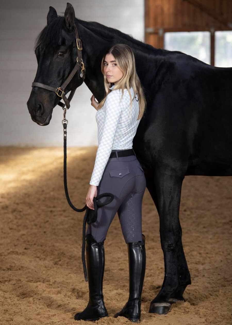 Woman standing beside a black horse in an indoor arena, dressed in equestrian attire.