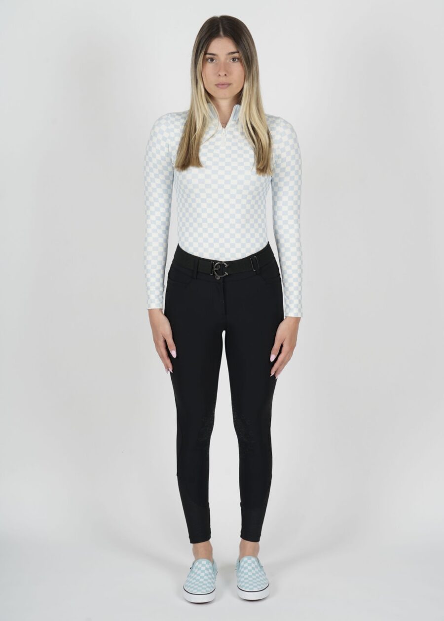 Woman in a white long-sleeve top and black pants posing against a plain background.