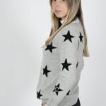 Woman wearing a gray sweater with black stars, standing sideways.