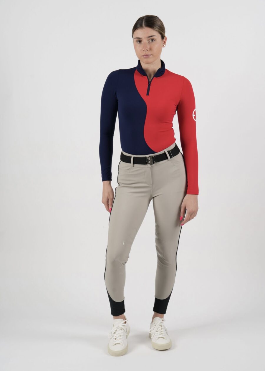 Woman wearing a color-blocked red and navy long-sleeve top with beige pants and black boots.