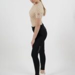 Woman in beige mesh top and black leggings posing sideways.