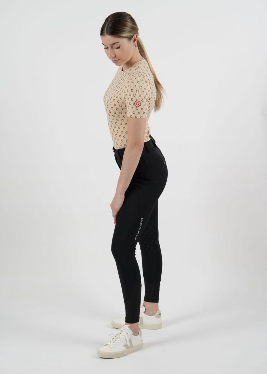 Woman in beige mesh top and black leggings posing sideways.