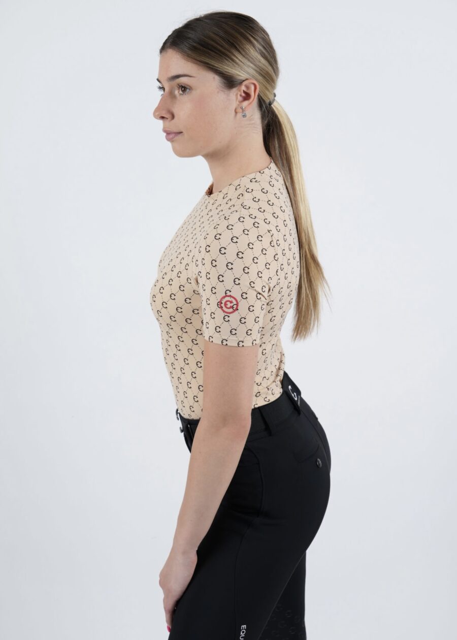 Woman in a beige patterned top and black pants standing sideways.