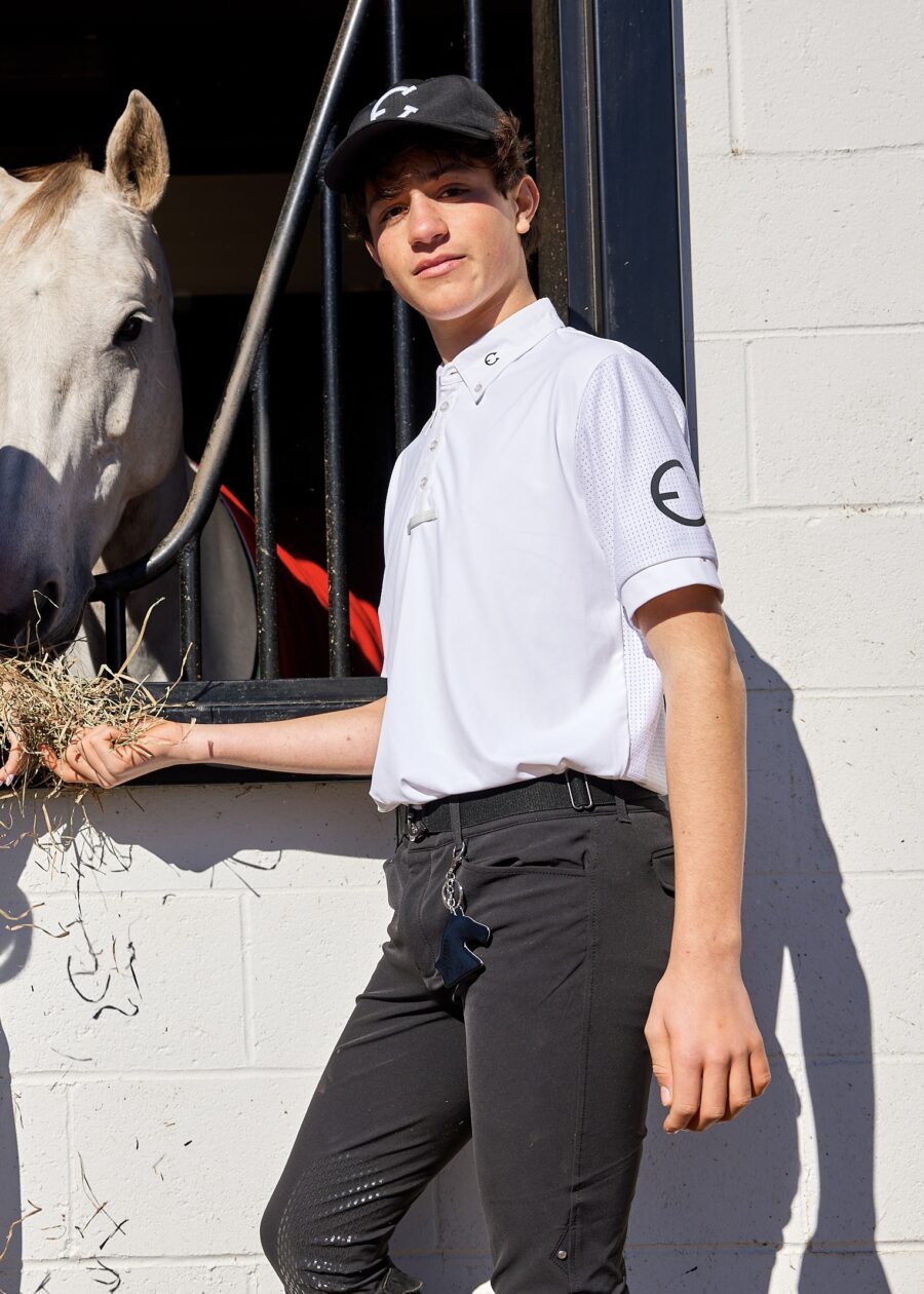 Young man feeding a white horse outside a stable.