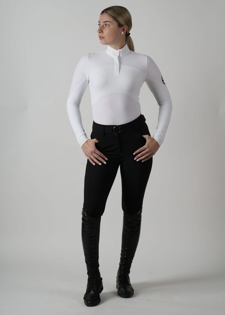 Woman in a white long-sleeve top and black pants posing confidently.