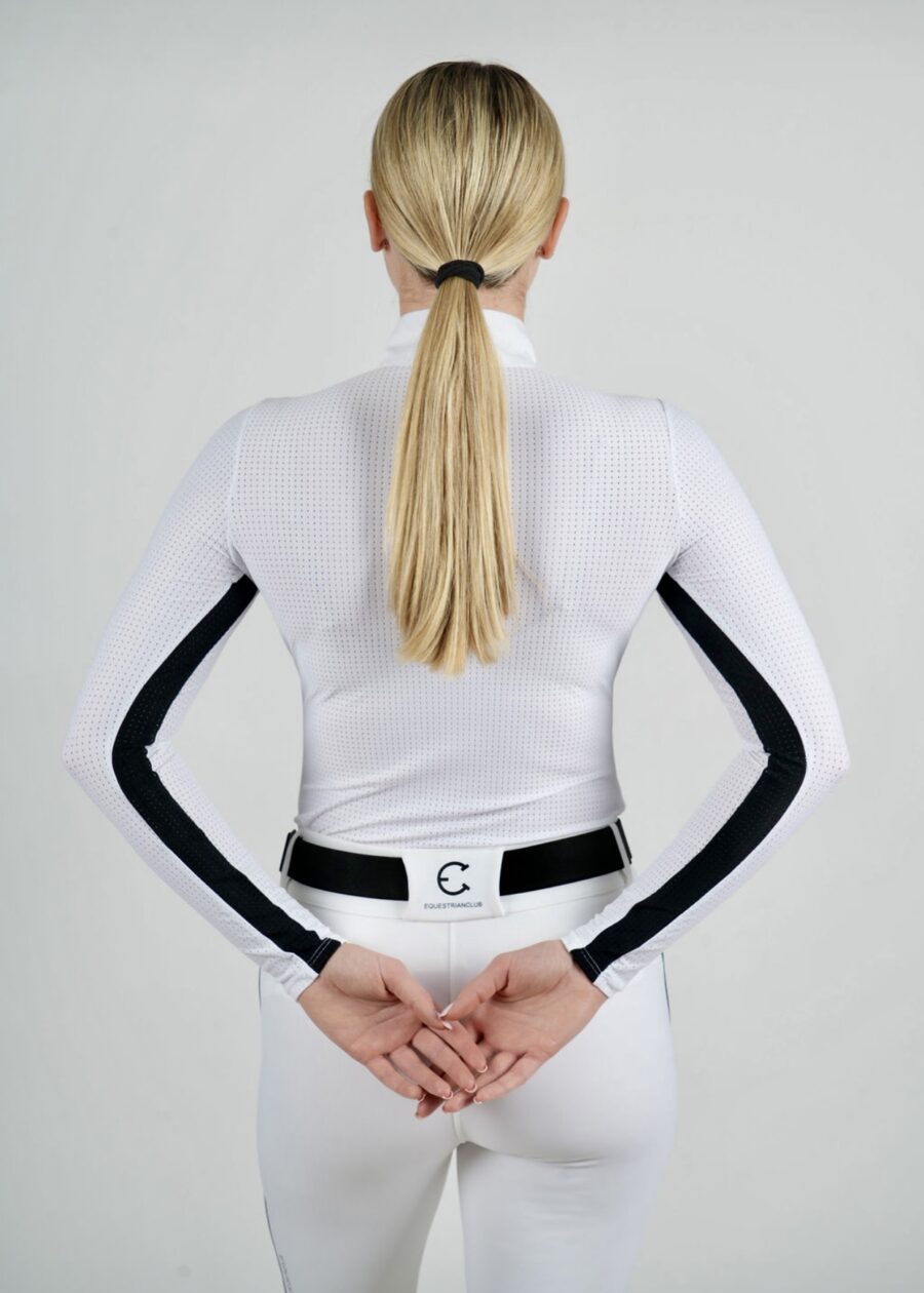 Rear view of a woman in a fitted white jacket with black stripes, hands clasped behind her back.